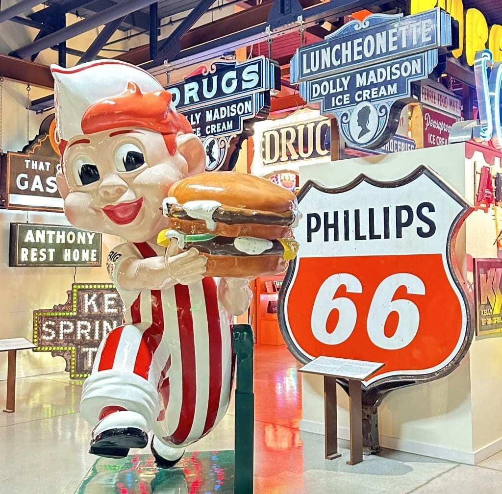 Vintage diner mascot holding a sandwich near a Phillips 66 sign.