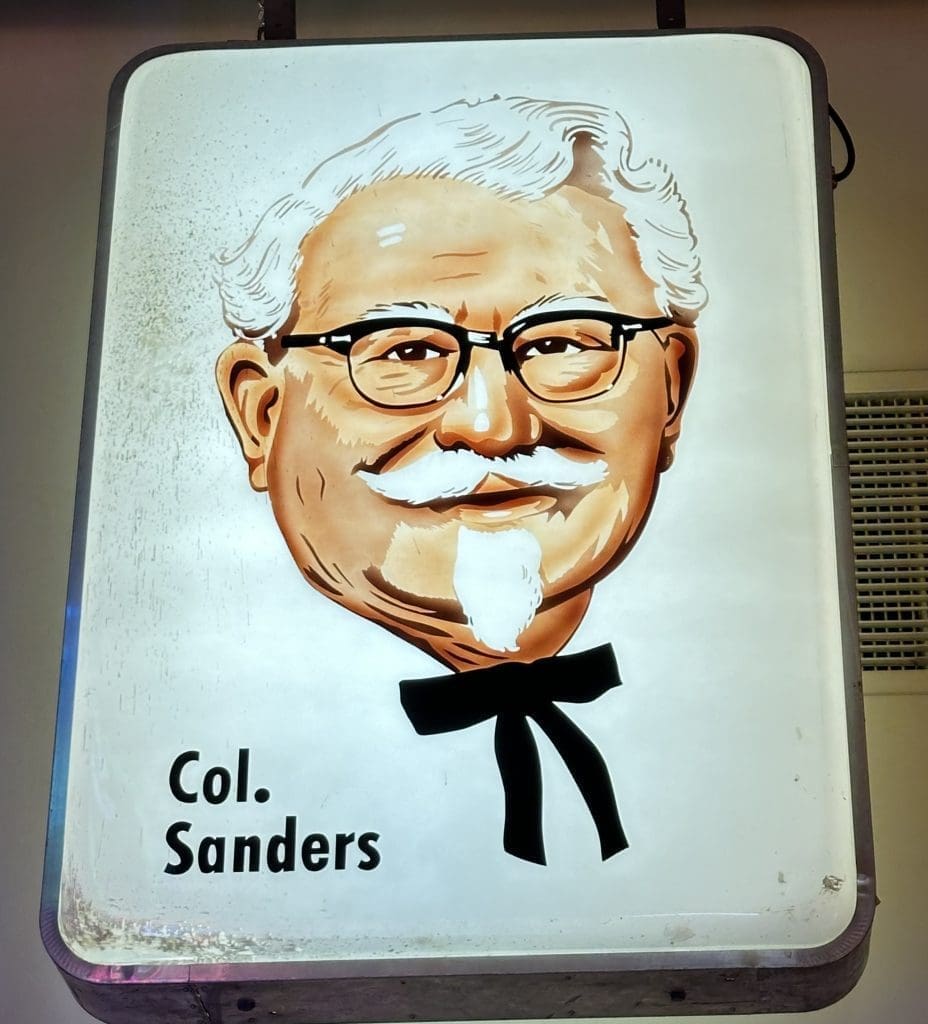A painted portrait of Col. Sanders with glasses and a bow tie.