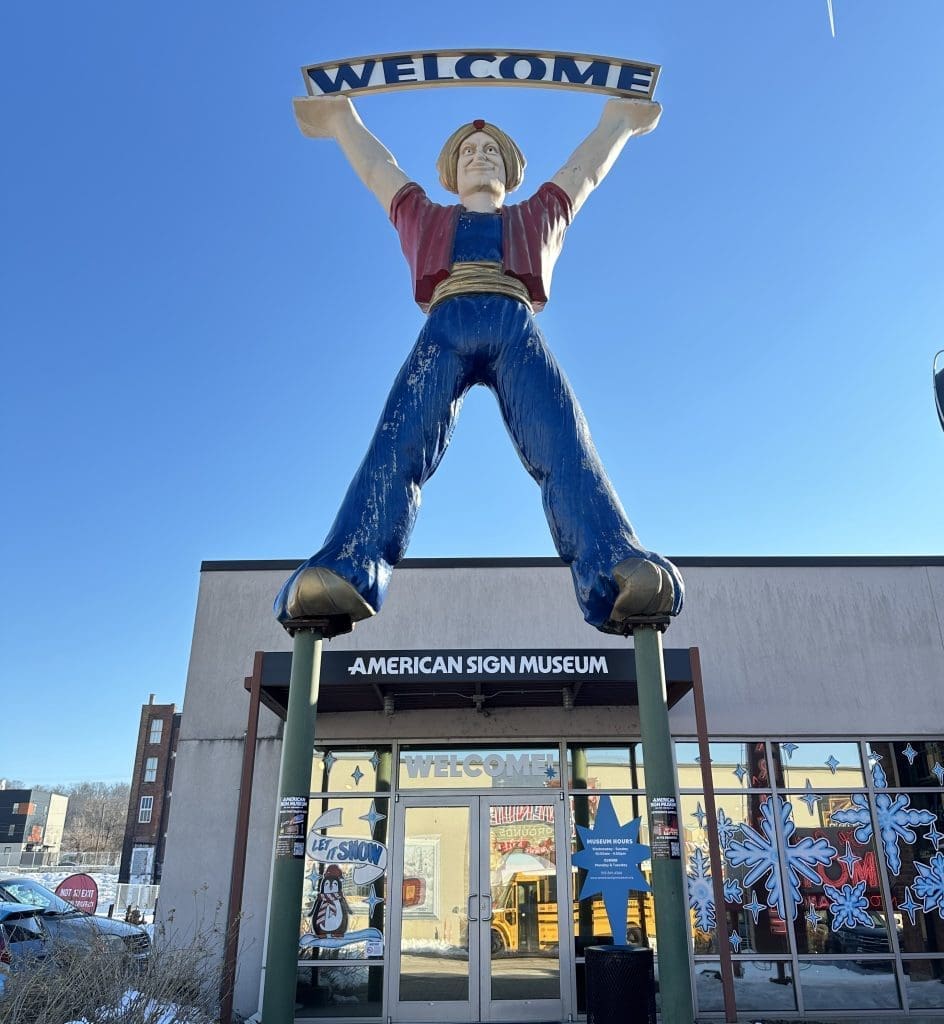 A giant statue of a man holding a 'Welcome' sign outside a store.