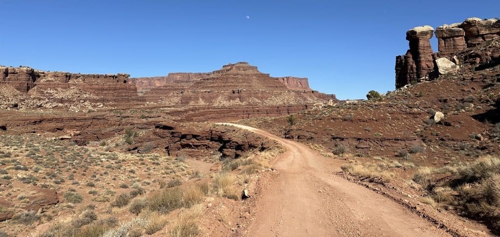 A dirt road winding through a rocky desert landscape under a clear blue sky.