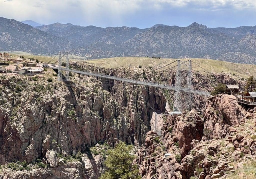 A long suspension bridge over a deep canyon with mountains in the background.