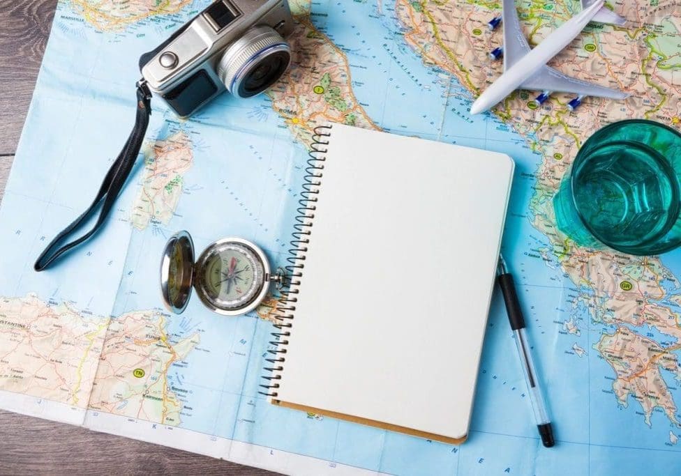 A blank notebook on a world map with travel items.